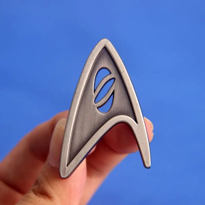 ST-Star X Trek Enamel Pin held up against a blue background, showcasing a classic logo design.
